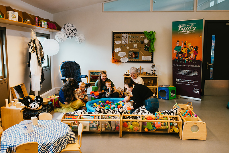 Parents with babies at a community centre, surrounded by baby toys