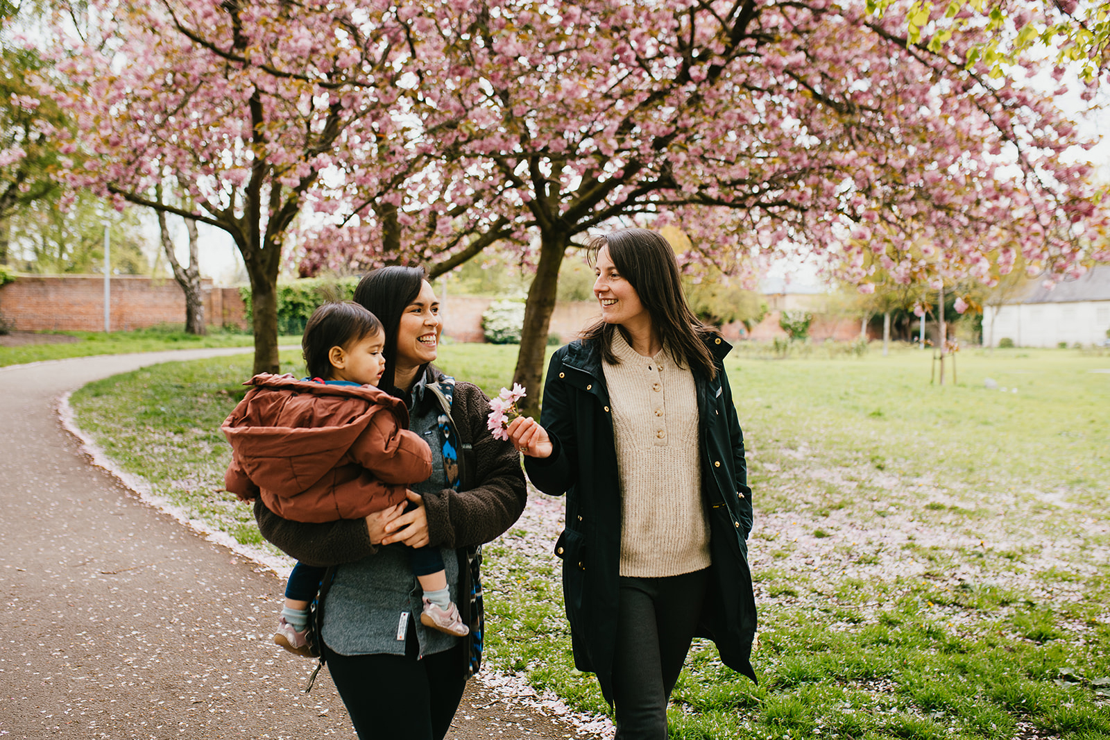 Two women walking in a park. One is holding a baby