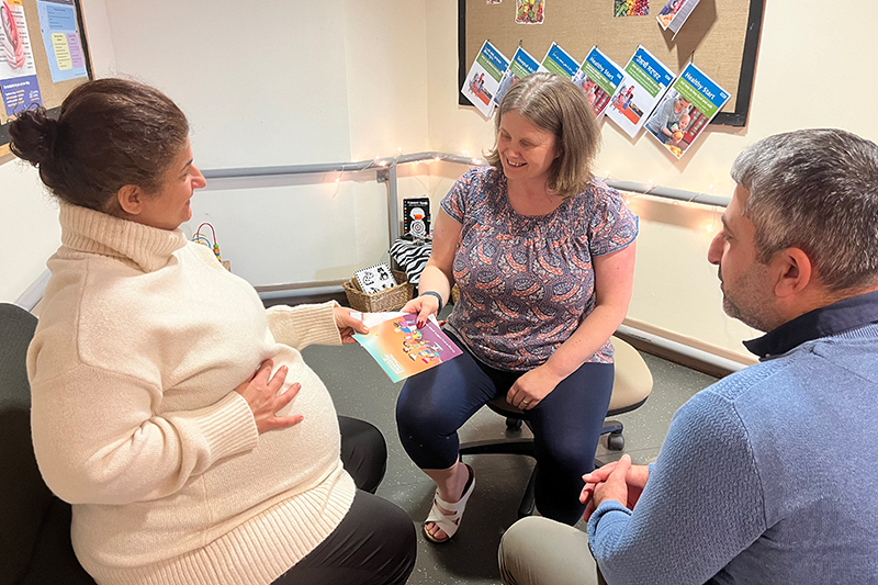 Support worker handing a booklet to a pregnant woman and her partner
