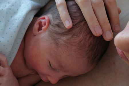 A mother lying with a baby wrapped in a blanket and asleep on her chest